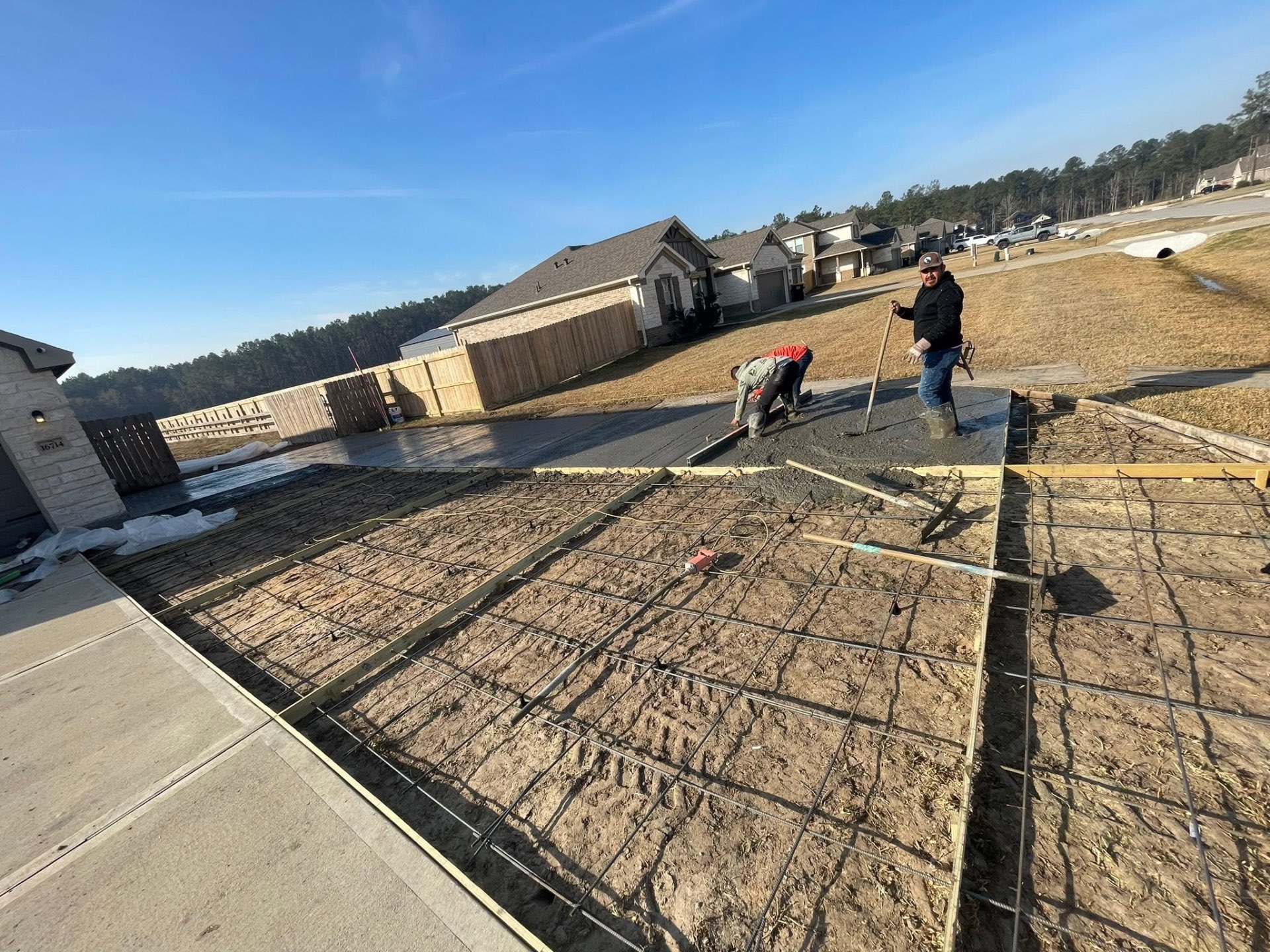 Crew finishing a large rebar-reinforced concrete driveway pour